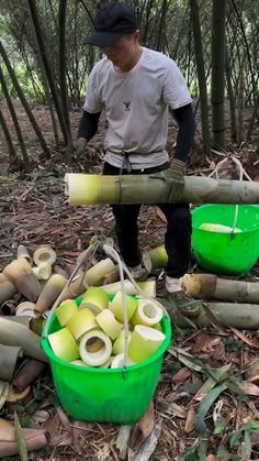 a man standing in the woods next to green buckets filled with apples and bamboo sticks