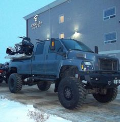 a large blue truck parked in front of a tall building with snow on the ground