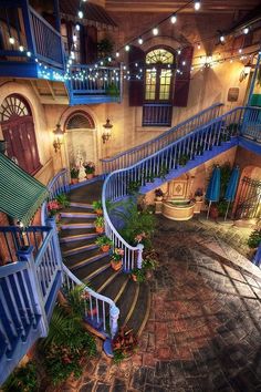 a spiral staircase in an old building with potted plants on the side and lights hanging from the ceiling