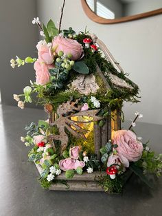 a birdhouse with flowers and greenery on the roof is sitting on a table in front of a mirror