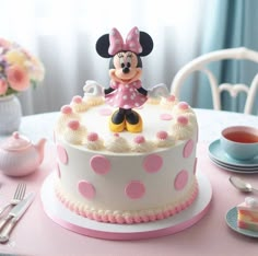 a minnie mouse cake sitting on top of a table next to a tea cup and saucer