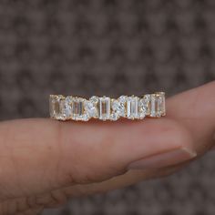 a woman's hand holding a gold ring with five baguettes on it