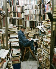 a man sitting on a stool in front of a large amount of books