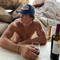 a shirtless man sitting at a table with a wine glass and bottle in front of him