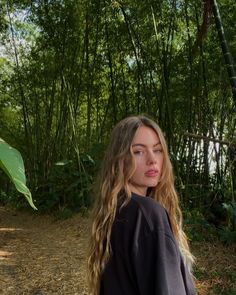 a woman with long hair standing in front of bamboo trees and looking off into the distance