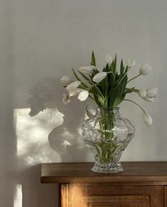 white tulips are in a clear vase on a dresser