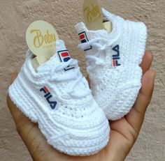 someone is holding two pairs of white knitted baby shoes with the word fila on them