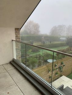 a balcony with glass railings overlooking a green yard and farm in the distance on a foggy day