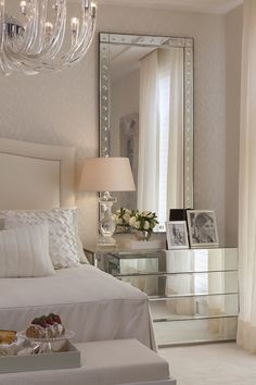 a white bed sitting next to a large mirror on top of a dresser in a bedroom