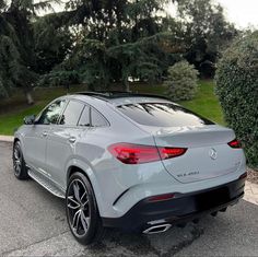 the rear end of a mercedes suv parked in a parking lot with trees and bushes behind it