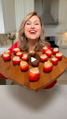 a woman holding a wooden tray with cupcakes on it in front of her face