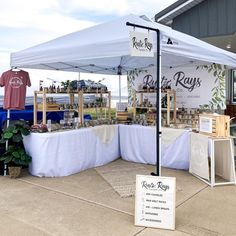 an outdoor market area with tables and chairs under a white tent that has plants on it