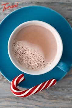 a cup of hot chocolate next to a candy cane on a blue plate with the word,