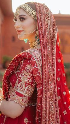 a woman in a red and gold bridal outfit is posing for the camera with her hand on her hip