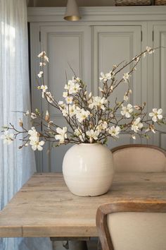 a white vase filled with flowers sitting on top of a wooden table next to a window