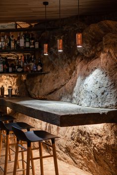 an empty bar with stools and bottles on the shelves in front of it, next to a stone wall