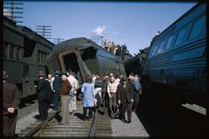 several people are standing on the train tracks as it pulls up to another train that is parked next to them