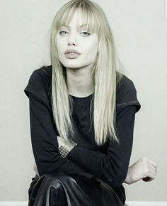 a woman with long blonde hair sitting on top of a black leather bag and looking at the camera