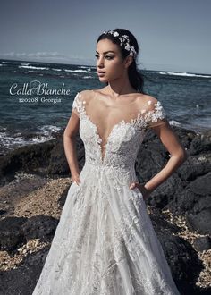 a woman in a wedding dress standing on the rocks by the ocean with her hands on her hips