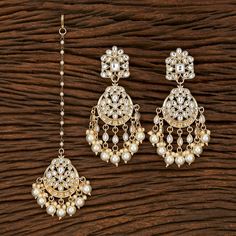 two pairs of earrings with pearls hanging from the side on a wooden surface, next to each other