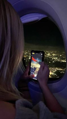 a woman is looking at her cell phone while flying in an airplane over the city lights