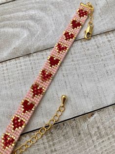 a pink beaded bracelet with red hearts and gold chains on a wooden table next to a pair of scissors