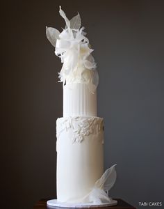 a three tiered white wedding cake with flowers on the top and bottom, sitting on a wooden table