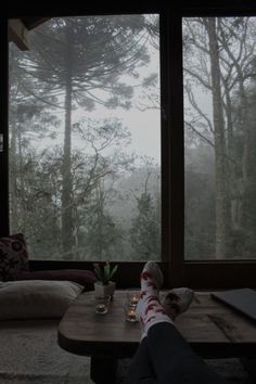 a person's feet resting on a coffee table in front of a large window