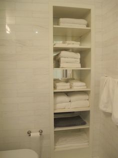 a white toilet sitting next to a bathroom shelf filled with towels and folded up sheets