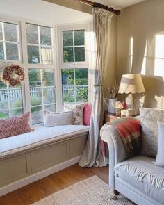 a living room filled with lots of furniture next to a window covered in curtains and pillows