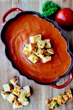 a red bowl filled with sauce and cubed tofus on top of a wooden table