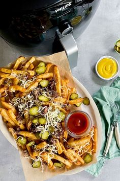 a plate full of french fries with cheese and olives next to an air fryer