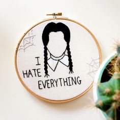 i hate everything embroidered on a hoop hanging next to a potted cacti