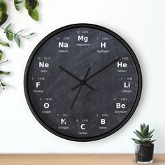 a clock with the names of different chemicals on it next to a potted plant