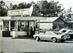 an old black and white photo of people standing in front of a store with cars parked outside