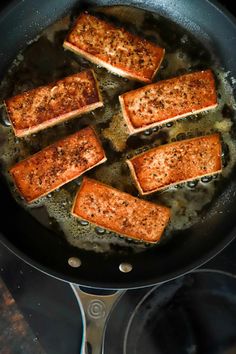 salmon being cooked in a skillet on top of a stove with oil and seasoning