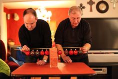 two men standing over a wooden table with ornaments on it