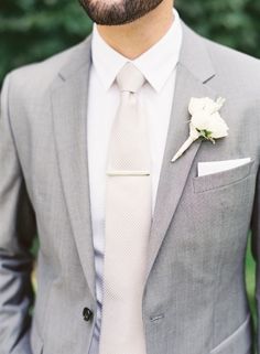 a man in a gray suit and white tie with a boutonniere on his lapel