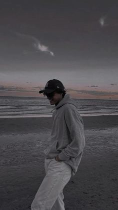 a man standing on top of a sandy beach next to the ocean under a cloudy sky