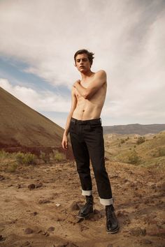 a shirtless man standing in the dirt with his hands on his hips and looking at the camera