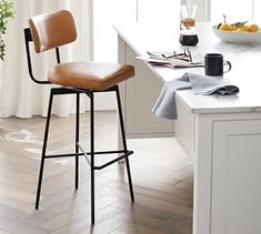 a kitchen with white counter tops and wooden flooring, along with a bar stool that has a brown leather upholstered seat