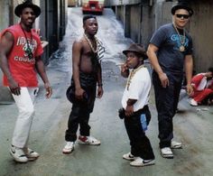 four young men standing in the middle of an alleyway, one wearing a hat