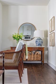 a living room with white walls and wood floors, a mirror on the wall above a wicker bench