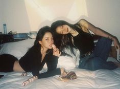 two young women laying on a bed with food in their hands and one is eating