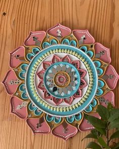 a decorative wall hanging on the side of a wooden table next to a potted plant