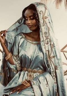 a woman in a blue and gold dress is holding her veil over her head while posing for the camera