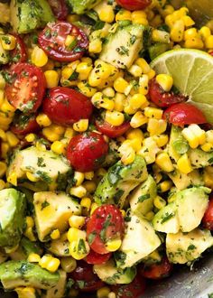 a bowl filled with corn, avocado and tomatoes next to lime wedges