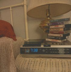 a stack of books sitting on top of a bed next to a lamp with a clock