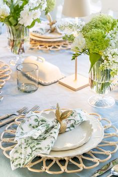 the table is set with plates, silverware and flowers in vases on it