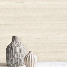 two vases sitting next to each other on a white counter top with a beige wall in the background